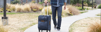 Man rolling a Whidbey carry-on suitcase on a paved alley.