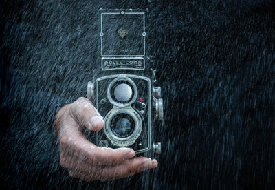 Man's hand holding a camera in the rain.