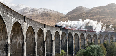 train seen coming on a bridge, against a mountainous backdrop.