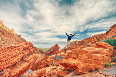 Young woman jumping happily on a rocky red canyon, blue skies in the background..